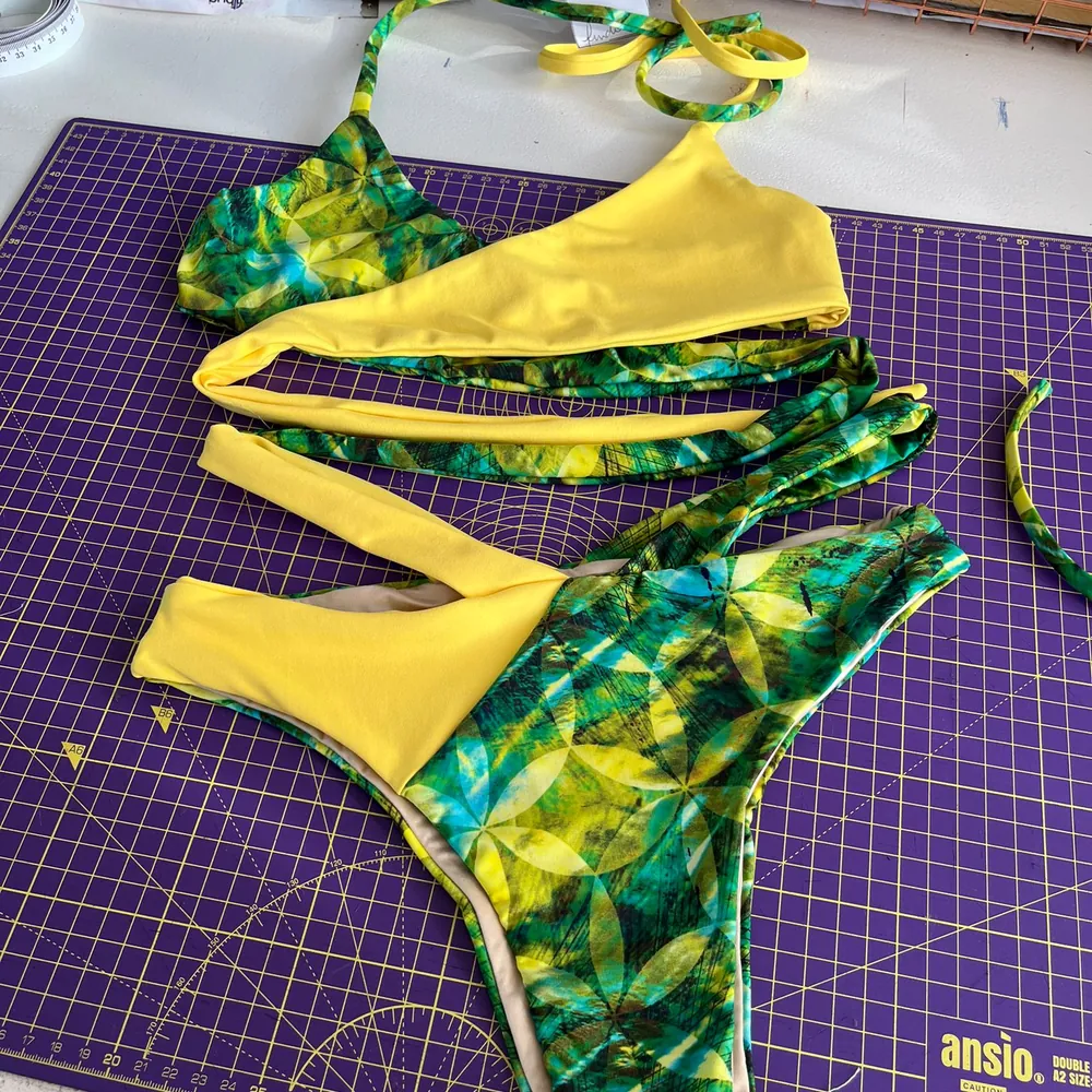 A bikini in yellow and a green tropical print, laid out on a cutting mat