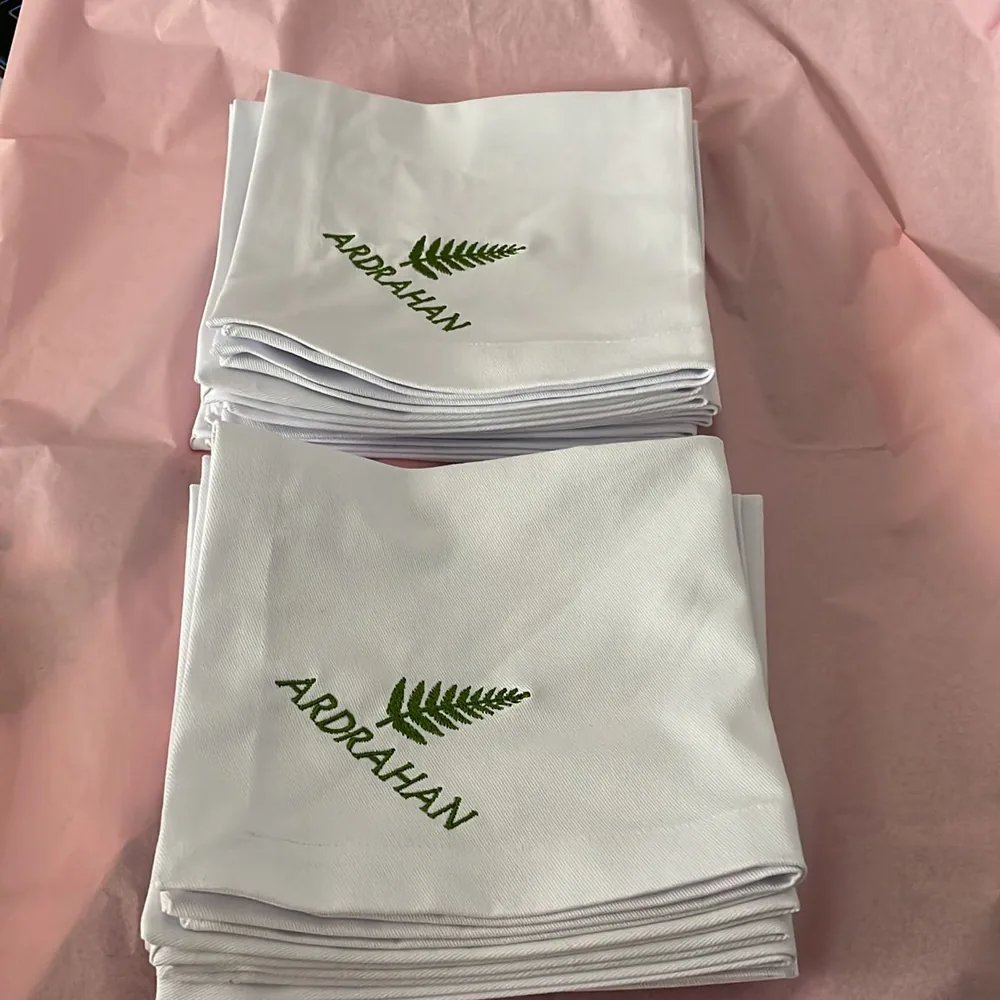 A stack of white cotton pieces, each embroidered with a green fern